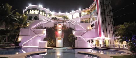 A multi-story hotel with a central staircase, a swimming pool, and a tall tower.