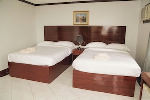 A hotel room with two wooden beds, white linens, a nightstand with a lamp, and a framed picture on the wall.