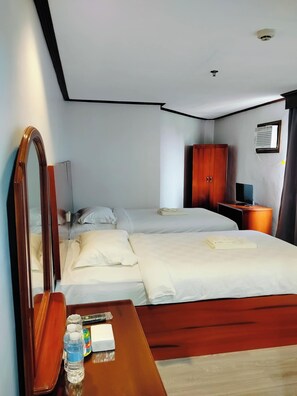 A hotel room with a bed, a wooden nightstand, a mirror, a wardrobe, and a window with curtains.