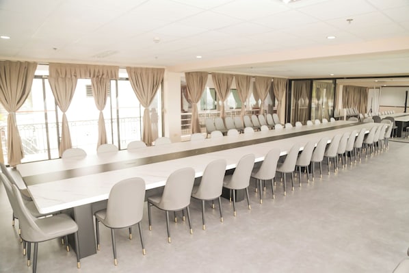 A conference room with a long table and chairs, large windows with curtains, and a balcony.