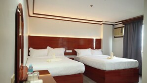 Habitación de hotel con dos camas, cabecera de madera, mesita de noche con lámpara y un espejo.