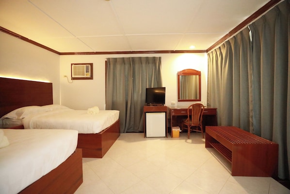 A hotel room with two beds, a desk, a chair, a TV, and a bench. - Bohol Plaza Resort and Restaurant (Dauis)