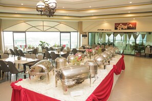 A buffet setup in a hotel function hall with multiple serving stations, chairs, and tables arranged for guests.