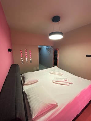 Quarto com cama, mesas de cabeceira, luminária pendente e parede decorativa.