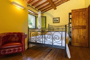 A bedroom with a metal bed frame, a red leather chair, a wooden door, and a bookshelf. - Villa Gabriella Chianti Toscana (Greve in Chianti)
