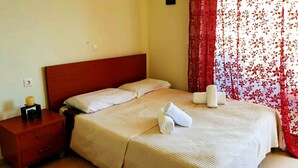 A hotel room with a bed, a nightstand, a lamp, and a window with floral curtains. - Homy Lovely House Near the Sea (Archanes-Asterousia)