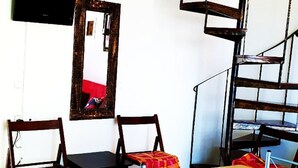 A dining area with a wooden table and chairs, a mirror on the wall, and a spiral staircase. - Homy Lovely House Near the Sea (Archanes-Asterousia)