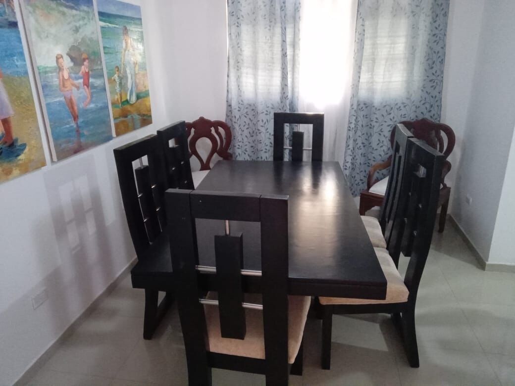 A dining area with a rectangular table and six chairs, each with a wooden frame and cushioned seats.
