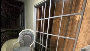 Quarto nos fundos com uma grande janela, uma mesa redonda pequena e duas cadeiras de vime com almofadas.