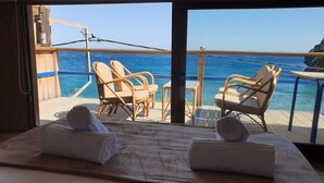 A balcony with two wicker chairs, a wooden table, and a view of the ocean. - Zacharias Luxury House On The Sea South Crete (Archanes-Asterousia)