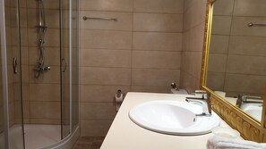 Une salle de bain avec une douche à parois de verre, un lavabo blanc, un miroir avec un cadre doré et une serviette posée sur le comptoir.
