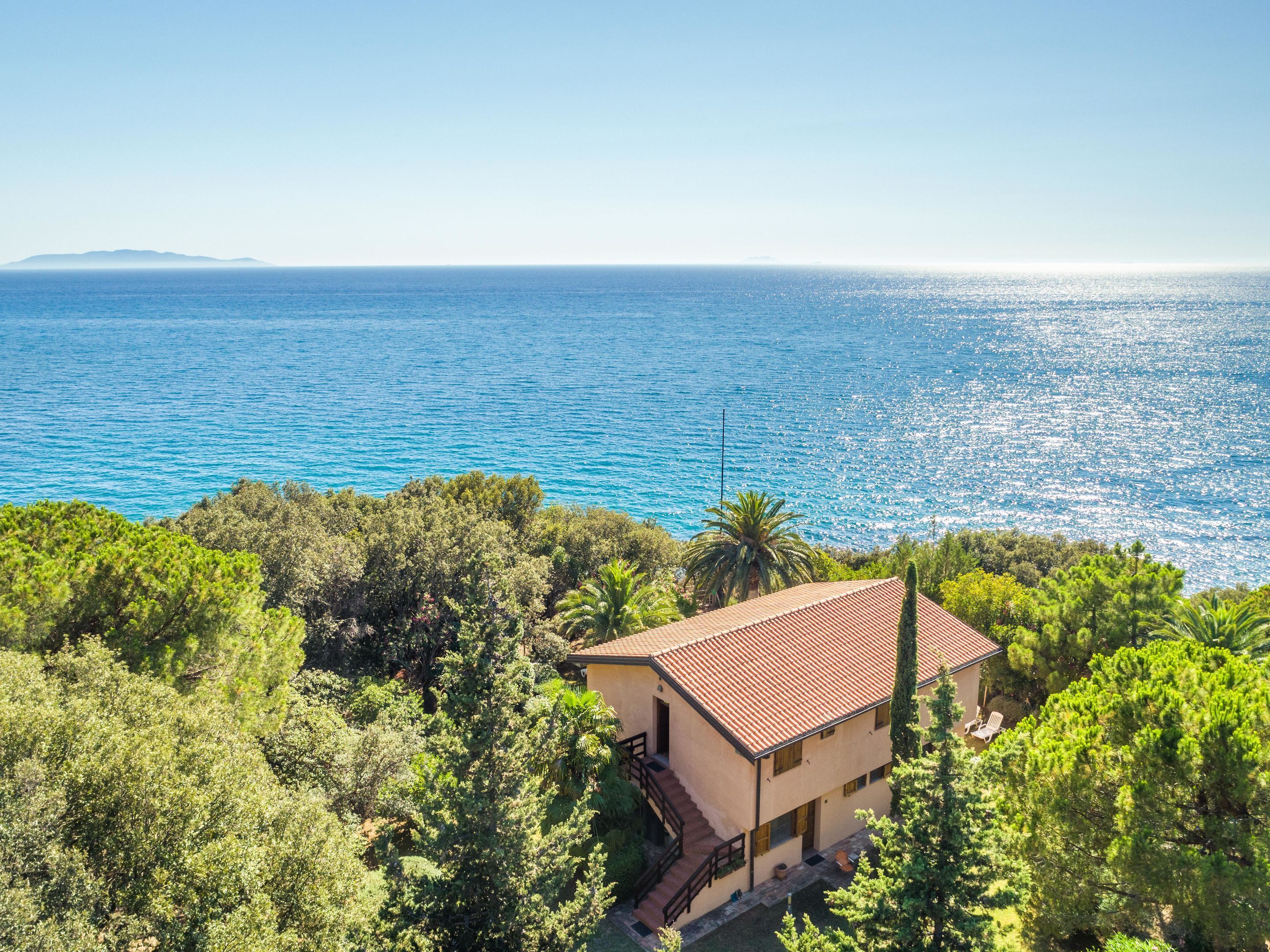 A coastal property with a sea view, surrounded by greenery, featuring a traditional building with a tiled roof.