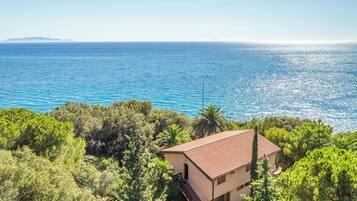 A coastal property with a sea view, surrounded by greenery, featuring a traditional building with a tiled roof.