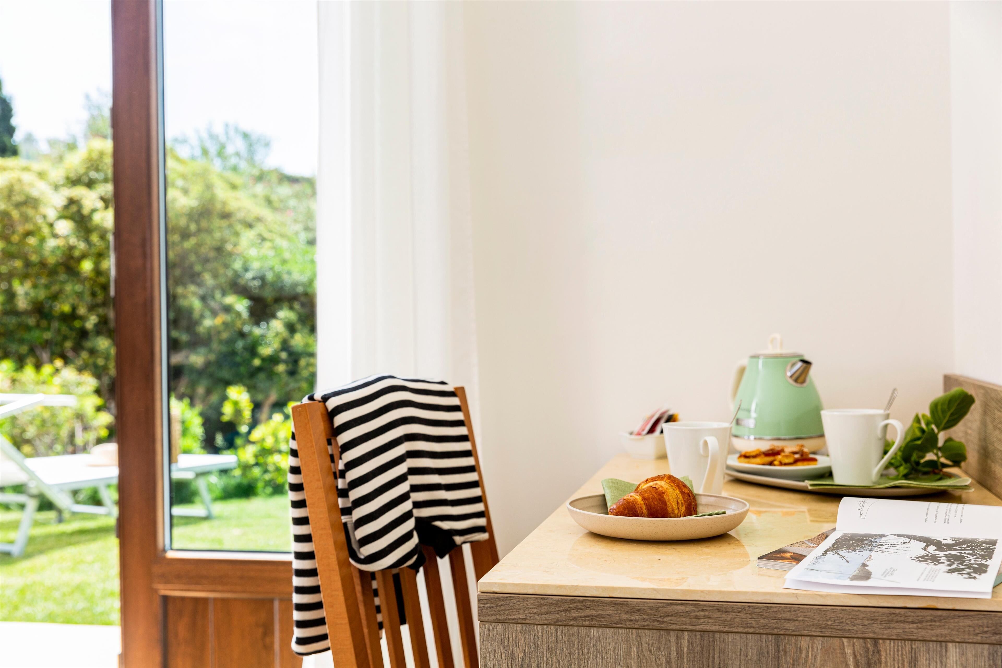 A breakfast table with a croissant, a green kettle, and a cup.