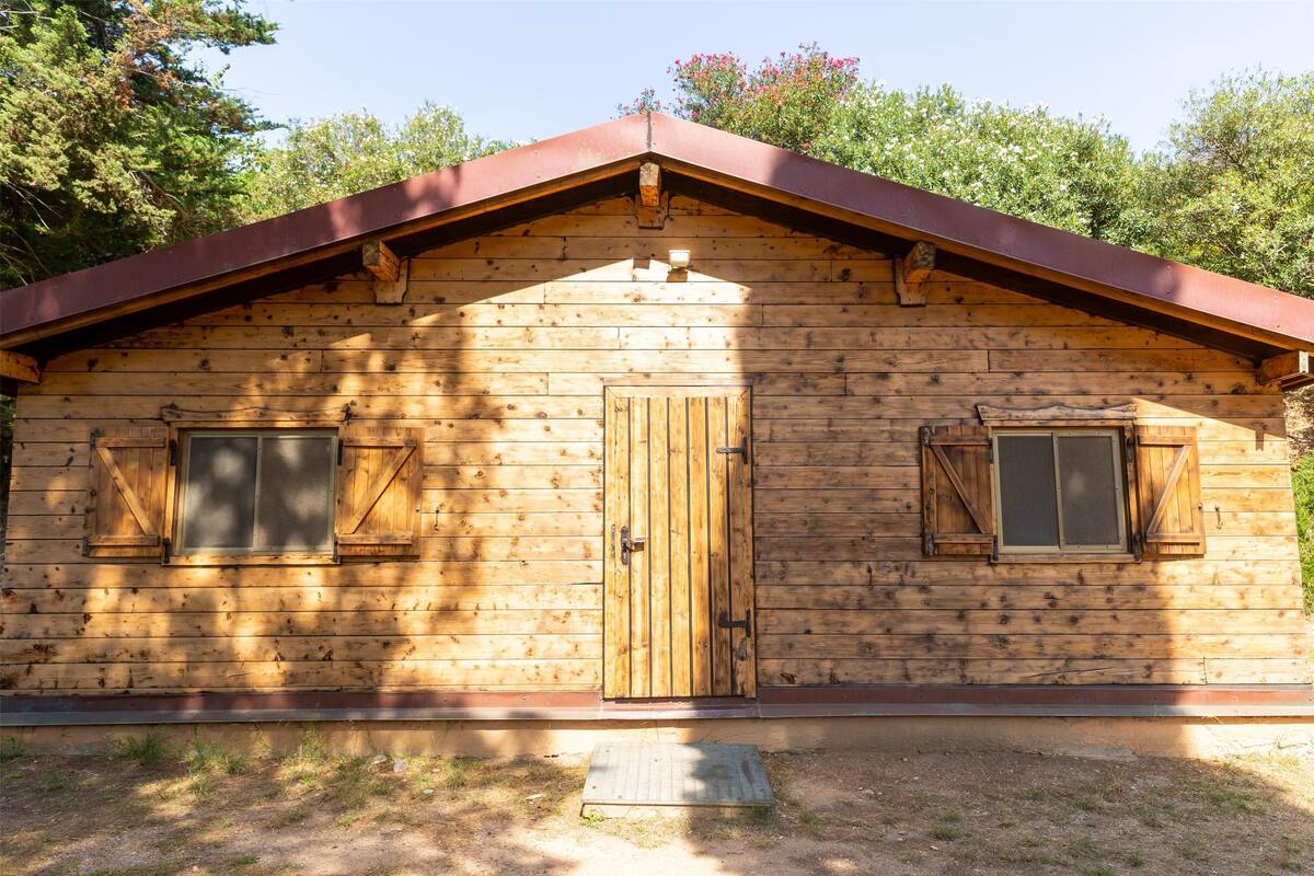 Una cabaña de madera con techo a dos aguas, dos ventanas con contraventanas y una puerta central.