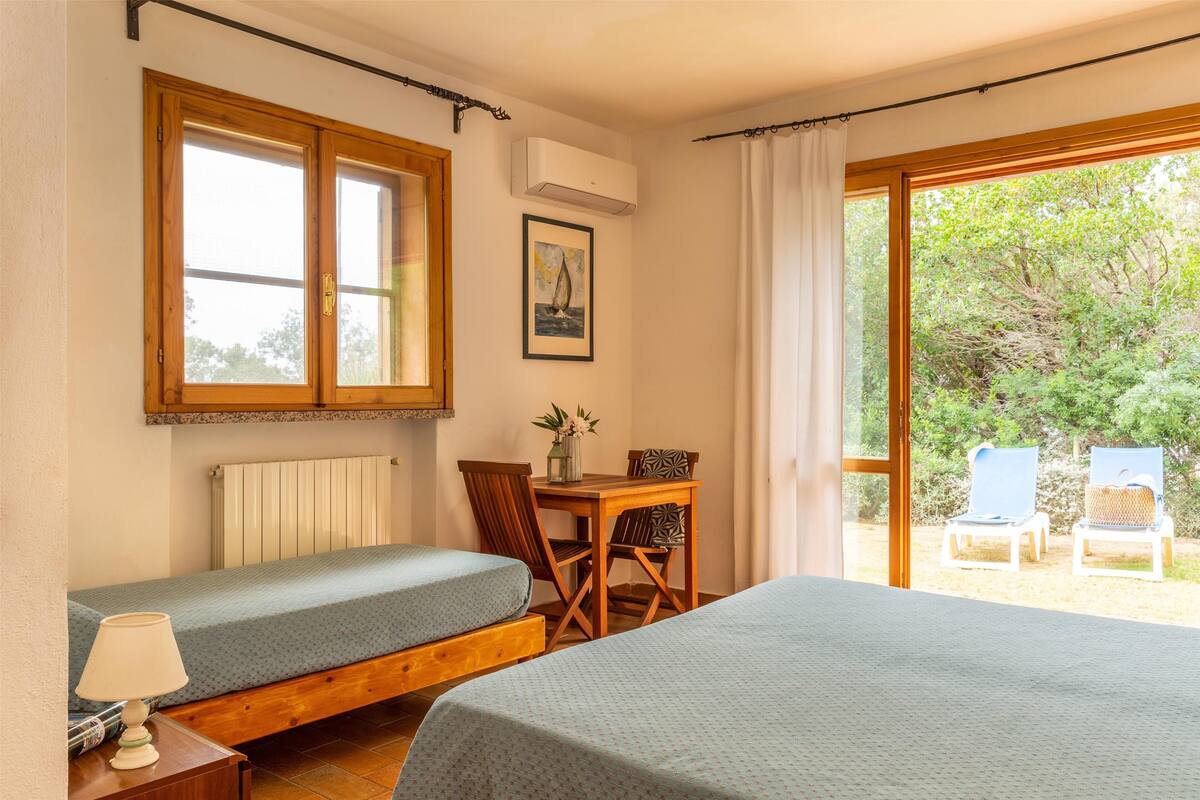 Un dormitorio con dos camas, una ventana, un radiador, una mesa con sillas y vistas al jardín.
