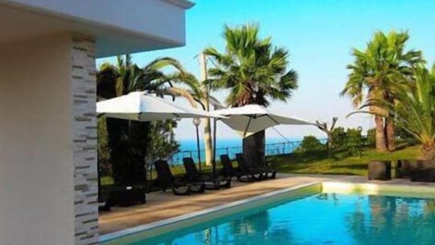 A swimming pool with lounge chairs and umbrellas, surrounded by palm trees and a clear sky.