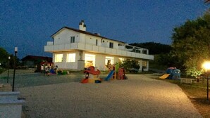 A two-story house with a driveway, a children's play area with slides and toys, and a well-lit exterior at dusk.