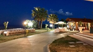 An outdoor dining area with tables and chairs, palm trees, and a building with a covered patio.