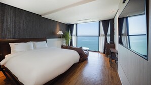A modern hotel room with a large bed, a small table, and a view of the ocean. - Hotel Urban Island (Namhae)