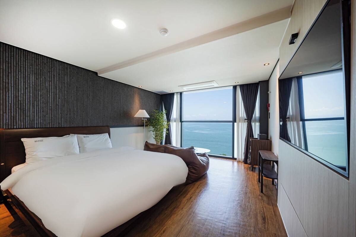 A modern hotel room with a large bed, a small table, and a view of the ocean.