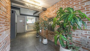 A hallway with brick walls, potted plants, and a modern light fixture. - Hotel Urban Island (Namhae)