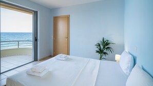 Quarto de hotel com uma cama, uma porta, uma planta e vista para o mar.
