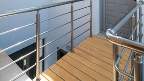 Escada de madeira com grades de metal que leva a uma porta com janela acima.