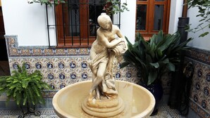 A stone fountain with a statue, surrounded by patterned tiles and potted plants. - Casa Museo La Merced (Málaga)