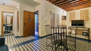 A room with a checkered floor, a wooden door, a television, and a metal chair. - Casa Museo La Merced (Málaga)