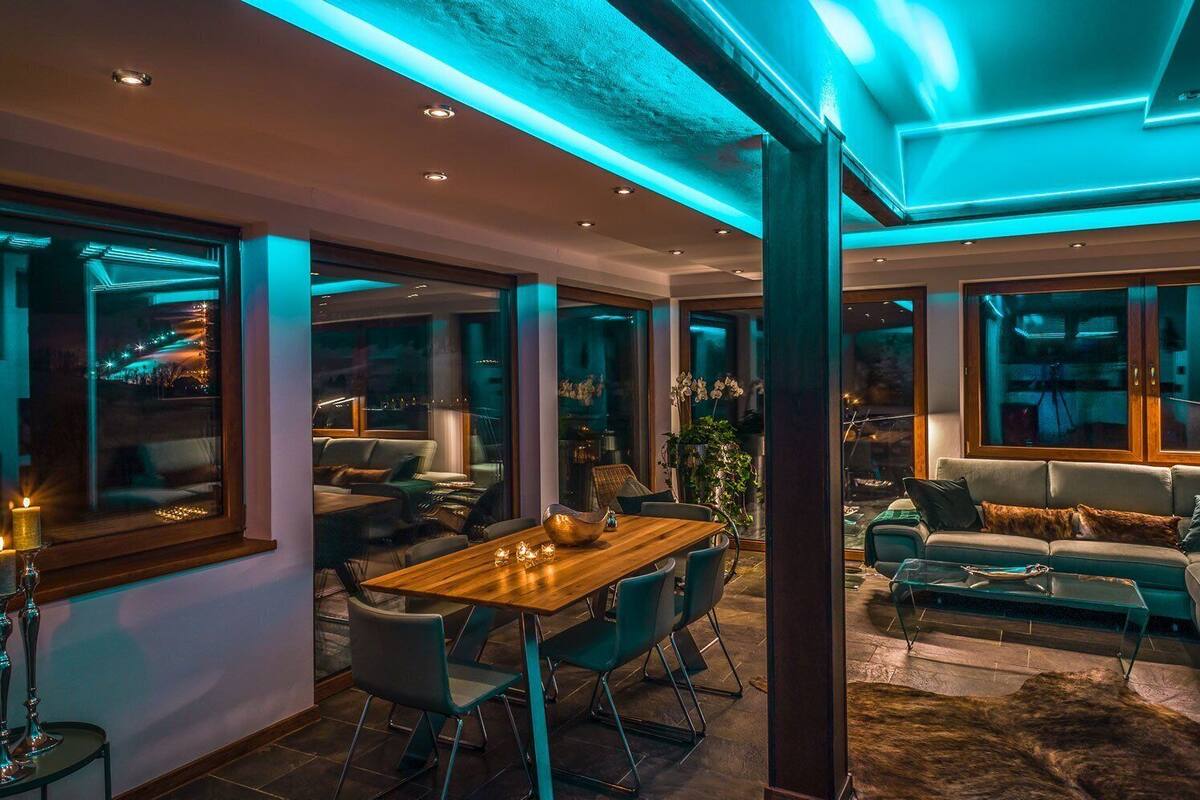 Ein modernes Wohnzimmer mit Esstisch aus Holz, bequemen Sitzmöglichkeiten und großen Fenstern mit Blick auf die Stadtlandschaft.