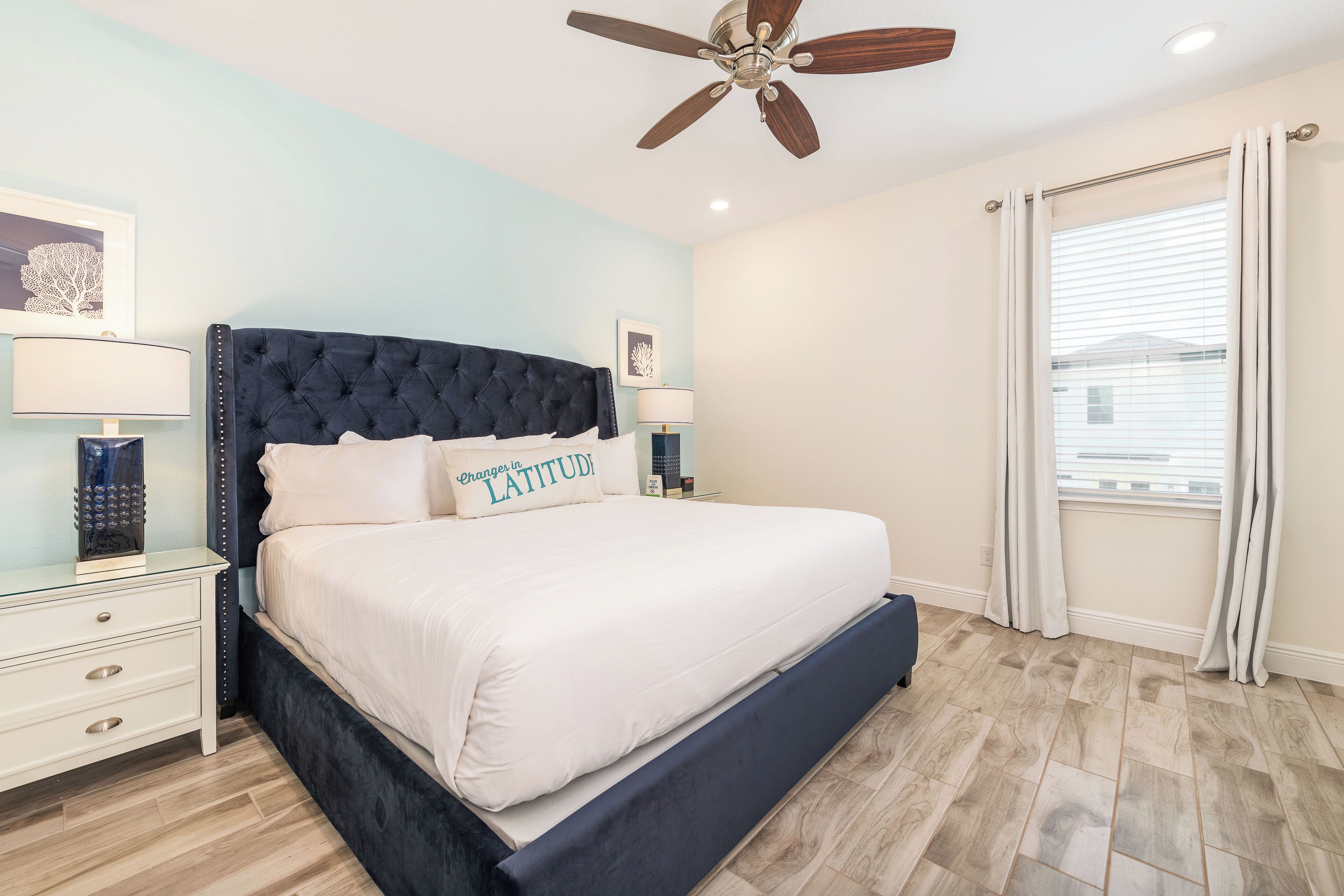 A bedroom with a large bed, two bedside tables, a ceiling fan, and a window with curtains.
