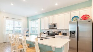 Una cocina moderna con armarios blancos, electrodomésticos de acero inoxidable y una isla central con sillas.