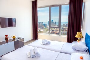 A hotel room with two beds, a flat-screen TV, a desk, and a view of a cityscape through large windows. - Panorama Baku - 22 Floor (Baku)
