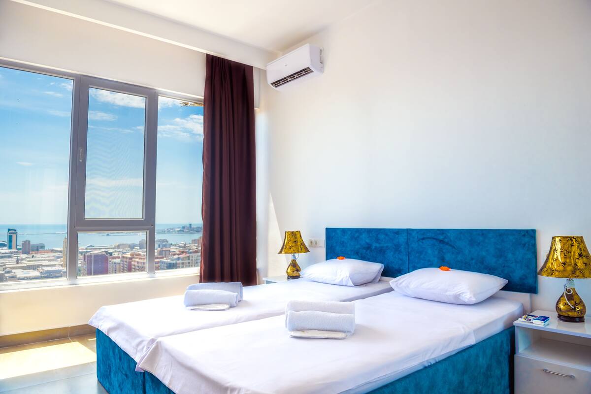 A hotel room with a large window, a bed with white linens, two bedside tables with lamps, and a view of the city.