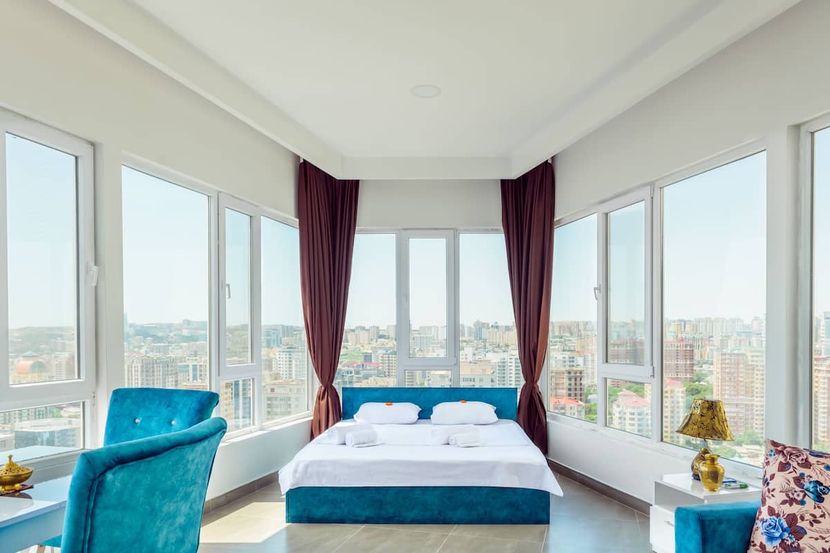 A hotel room with a large bed, a blue chair, a small table, and a view of the city.