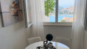 Un comedor con una mesa redonda, sillas blancas, una planta en maceta, una bandeja con una taza y un control remoto, y un cuadro en la pared.