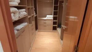 Um closet estreito com espaço para circulação, prateleiras de madeira, gavetas e porta com espelho.