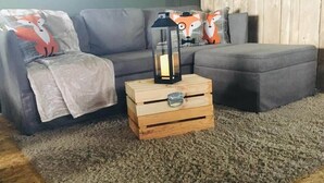 A living room with a grey sofa, a grey ottoman, a wooden chest with a lantern, and a shaggy rug. - Wingfield Escapes (Diss)