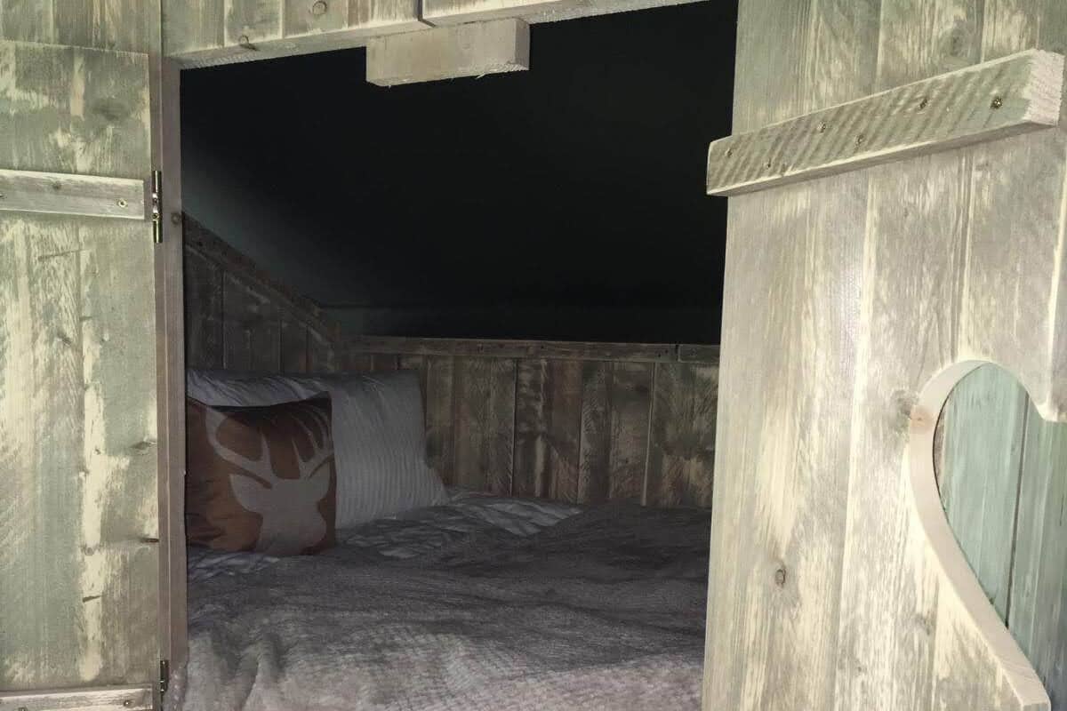 Une pièce rustique en bois, avec un lit en mezzanine, une petite fenêtre et une échelle en bois.