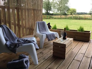 A wooden deck with two white plastic chairs, a wooden table with a bottle and glasses, and a wooden planter. - Wingfield Escapes (Diss)