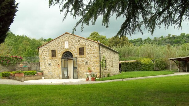 Un bâtiment en pierre avec un toit en tuiles, une entrée centrale et un petit jardin agrémenté de plantes en pot.
