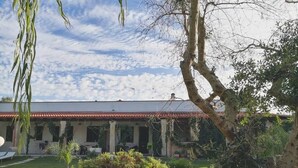 Um edifício com telhado de telhas vermelhas, rodeado por vegetação exuberante e céu claro.