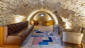 Ein Dachzimmer mit Steinwänden, einem braunen Ledersofa, gemusterten Sesseln und einem farbenfrohen Teppich.