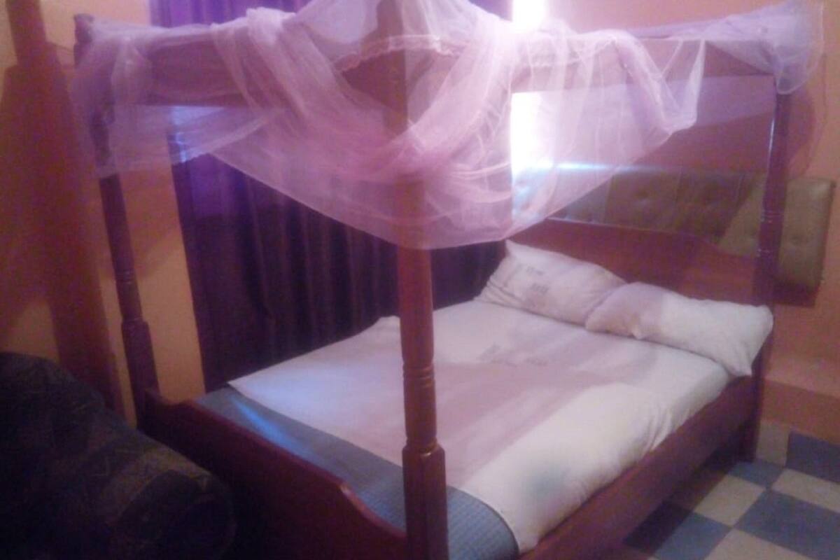 A single bed with a wooden frame, a canopy, and a checkered floor.