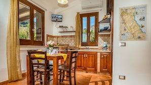 A kitchen with wooden cabinets, a dining table with chairs, a TV mounted on the wall, and a map on the wall. - Villa Elena 2 Km From the Natural Reserve of Zingaro (Castellammare del Golfo)