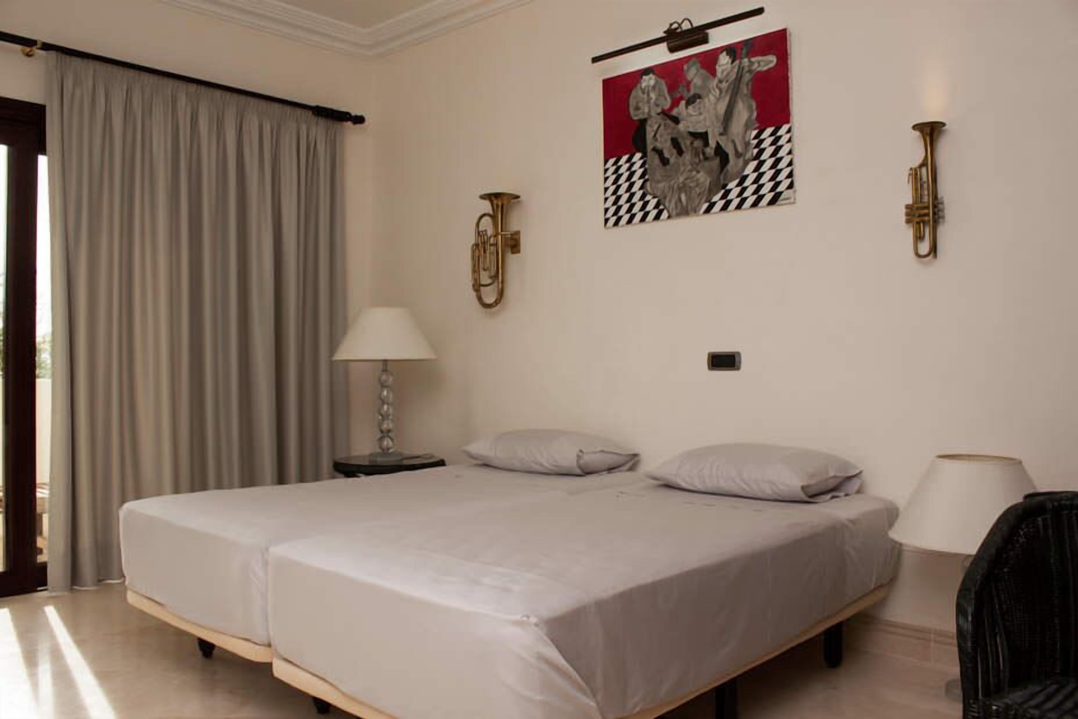Ein Hotelzimmer mit einem großen Bett, zwei Nachttischen, einer Lampe, einem Sessel und einem Bild an der Wand.