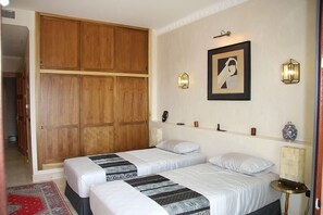 A bedroom with two beds, wooden wardrobe, wall-mounted lights, and a framed picture.