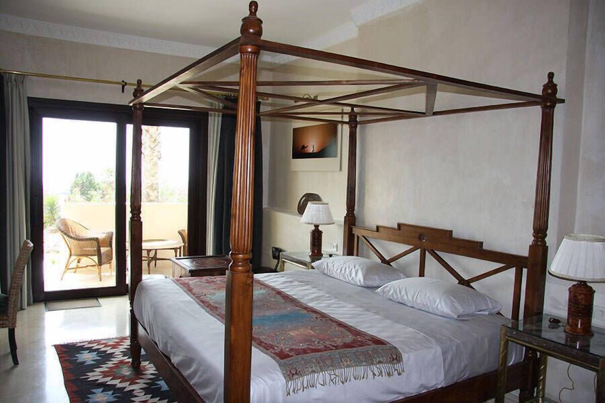 Una cama con dosel de madera, un edredón estampado y una mesita de noche con una lámpara.
