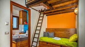 Een slaapkamer met een houten bed, een ladder, een houten garderobe en een badkamer met een spiegel en wastafel.